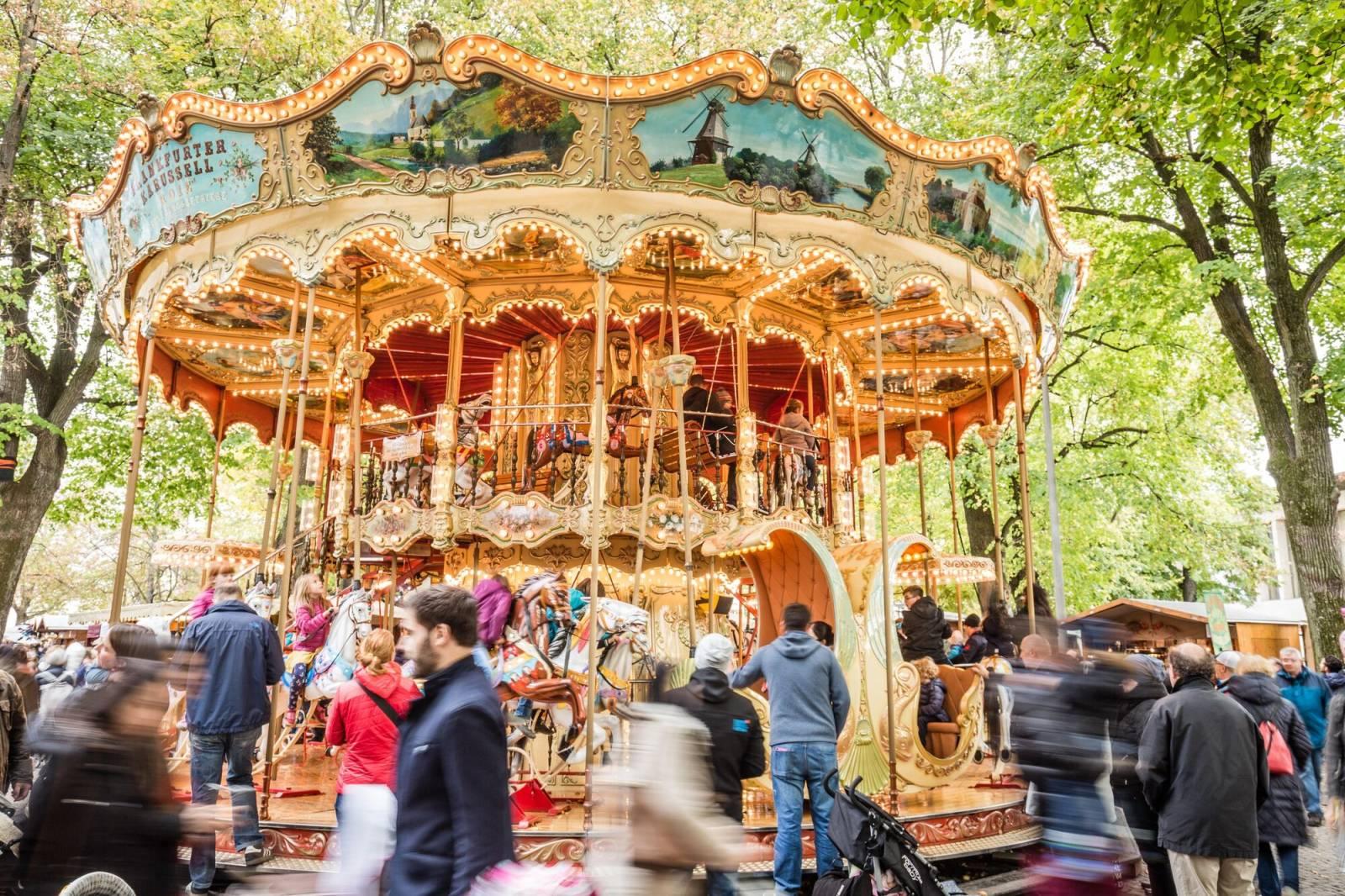 Des enfants tout sourire faisant du manège sur le traditionnel « Frankfurter-Pferdekarussell », magnifiquement décoré et illuminé, sous les grands tilleuls de la Petersplatz à Bâle.
